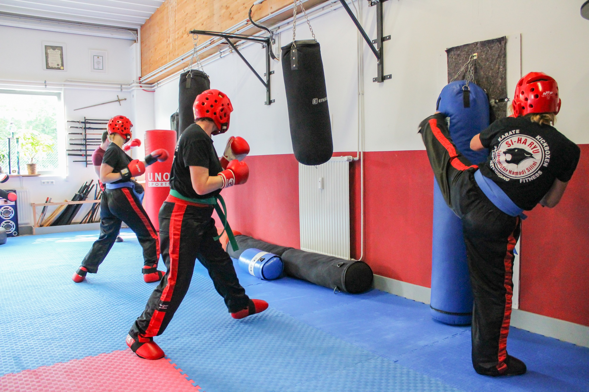 Vier Personen in Trainingskleidung trainieren Kickboxen an Boxsäcken